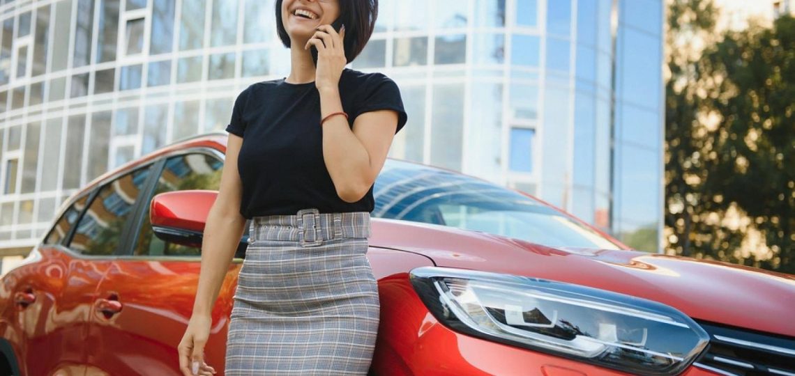 Woman standing next to a red rental car making a phone call outside a UAE building