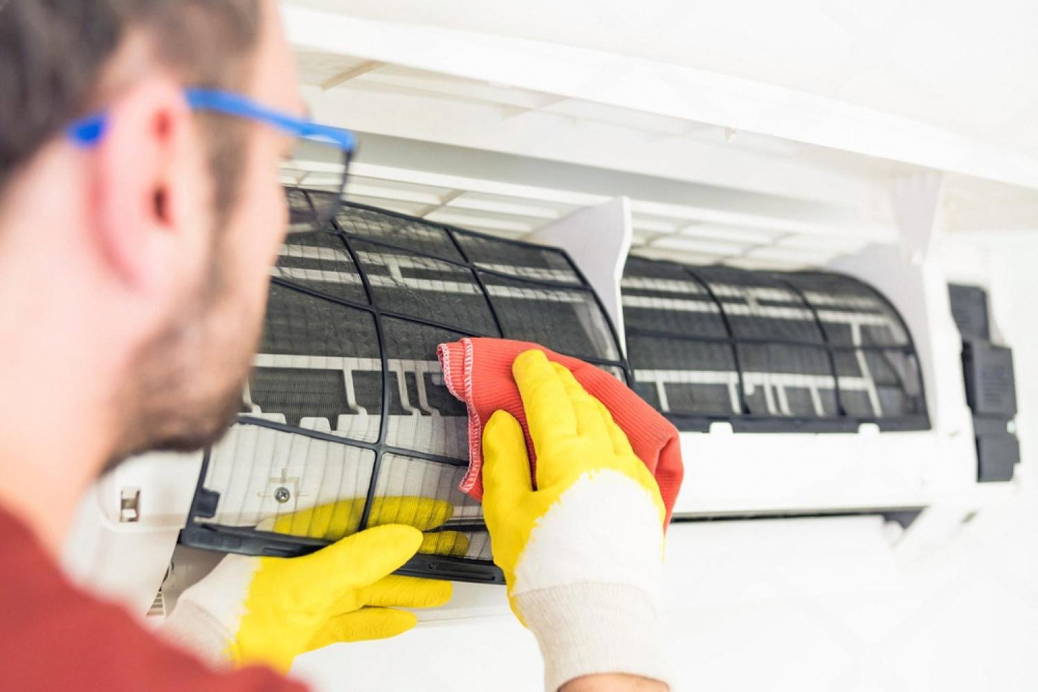 Technician in yellow gloves cleaning a mouldy split air conditioner unit in a UAE home