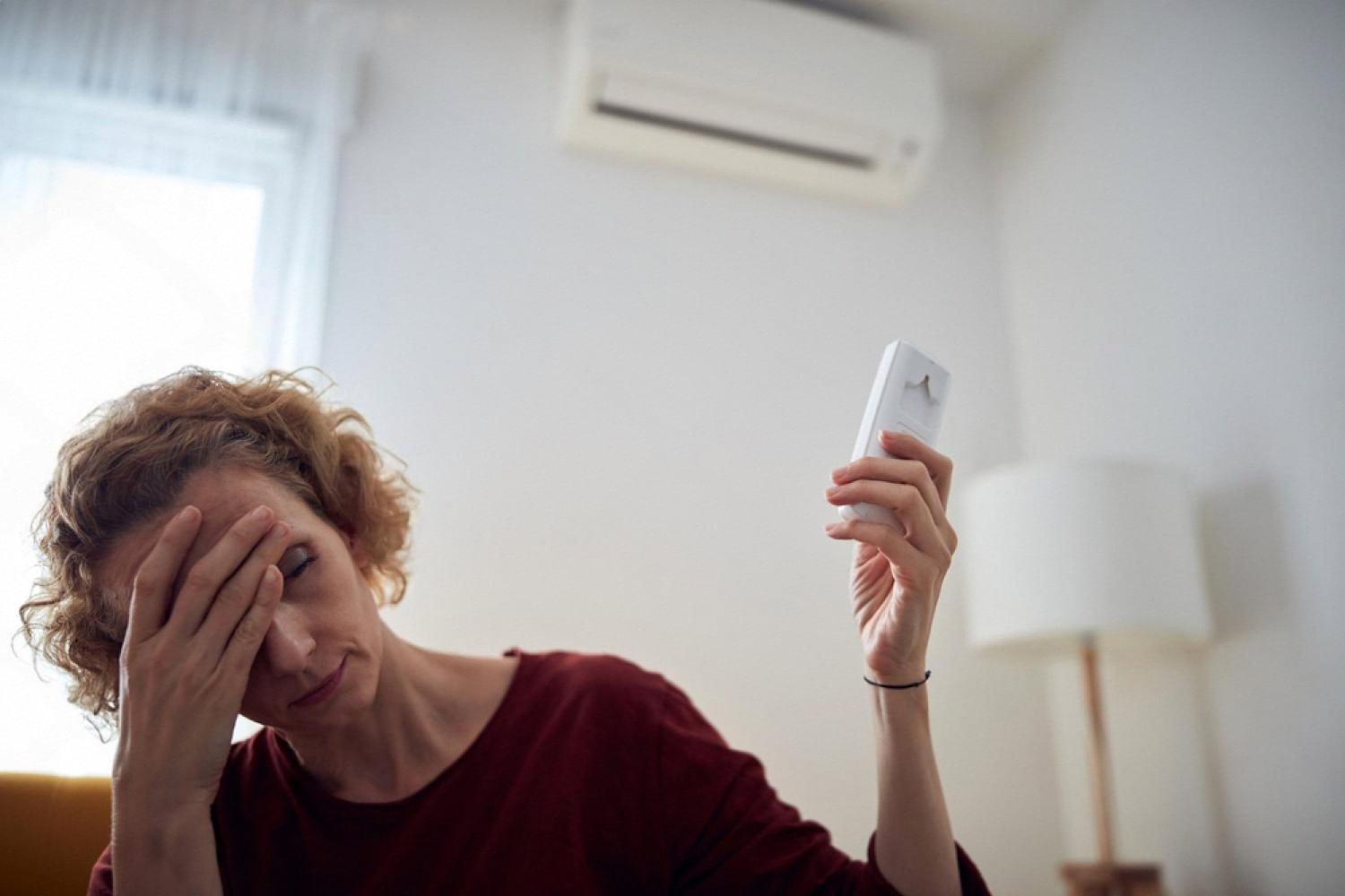 Woman holding an AC remote and covering her face because of a bad smell from the air conditioner