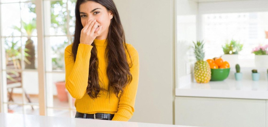 Young woman pinching her nose reacting to an unpleasant odour coming from an air conditioner